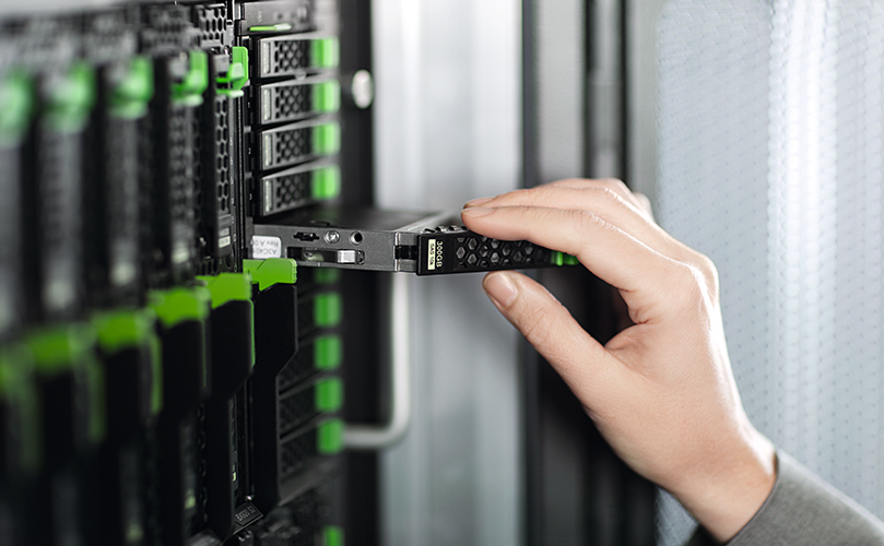 A hand inserting a storage drive into a server rack.
