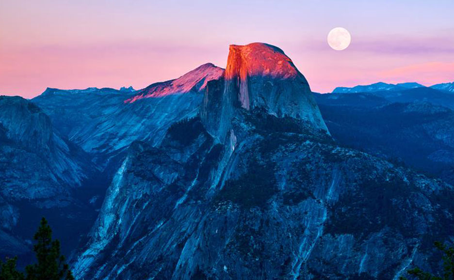 Majestic landscape with mountains tinged by sunset, full moon in sky.