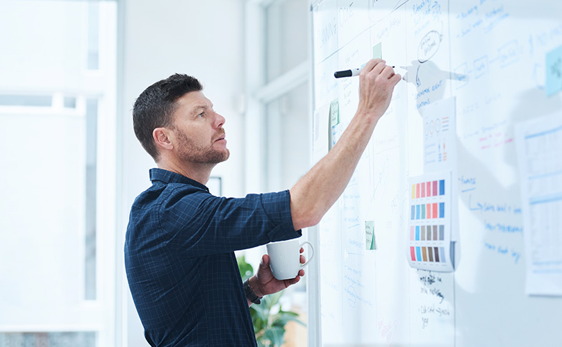 ホワイトボードに黒マジックペンで説明書きをする男性