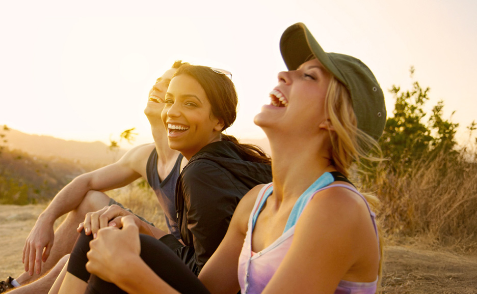 Three friends laughing together outdoors during sunset.