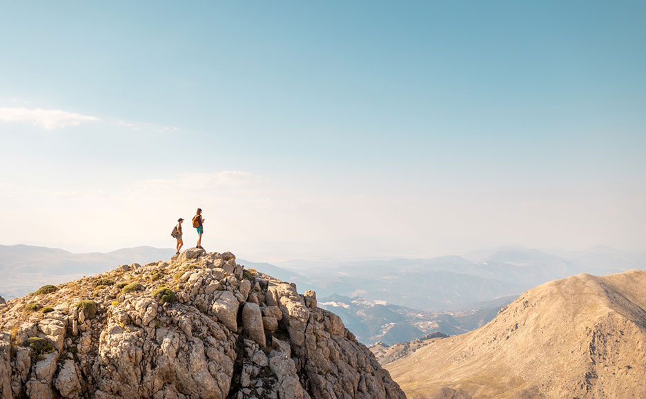 Two people standing on the top of the mountain, the view of the spreading mountains.