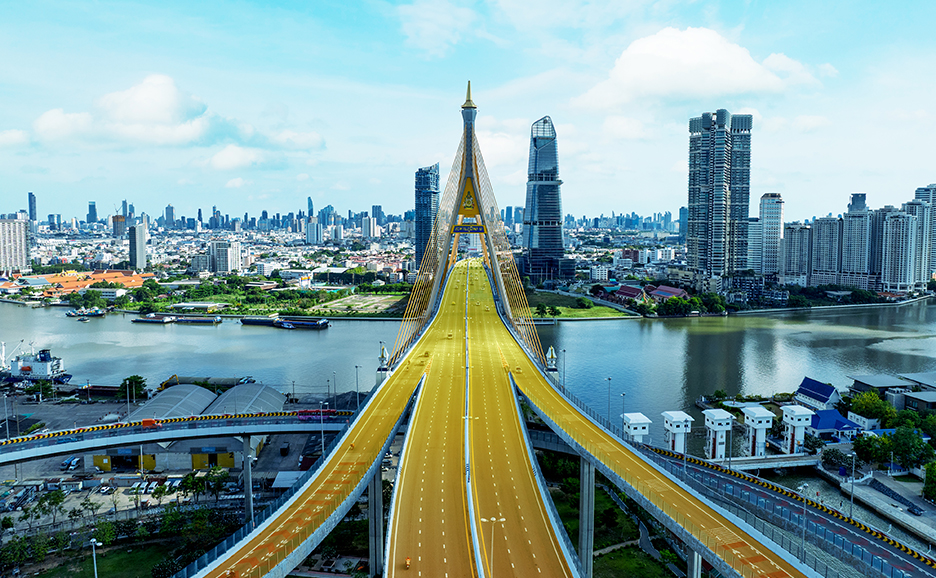 A modern cable-stayed bridge over a river, connecting cityscapes under a bright sky.