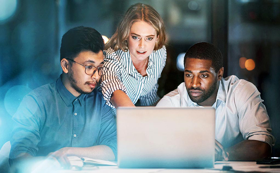 Three multi-ethnic business people working late around a PC