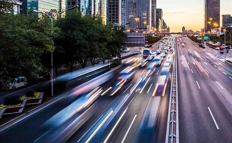 Light trails from vehicles moving along an urban highway at sunset.