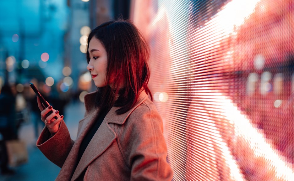 A woman looking at her phone in front of a brightly lit LED display.