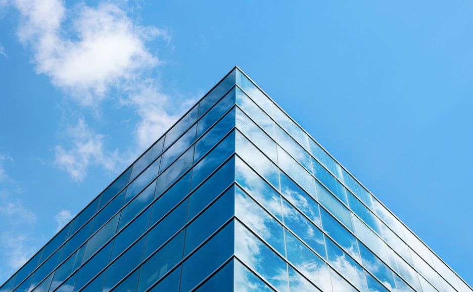 A low-angle shot of a modern glass building against a blue sky with clouds.
