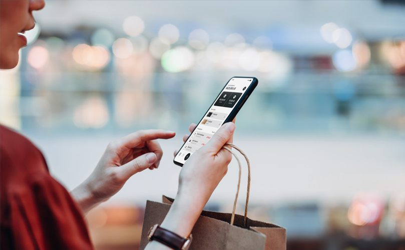 Naine kontrollib oma telefoni, ostukott käes