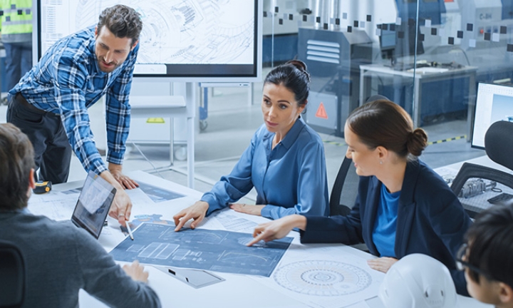 Several men and women in a meeting, pointing at something like a blueprint