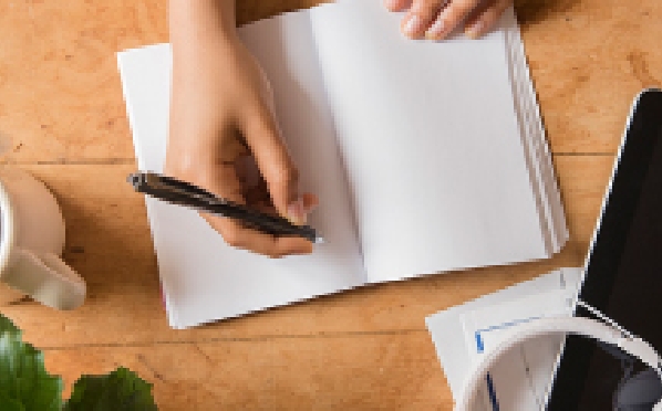An overhead view of a hand about to write something in a white notebook