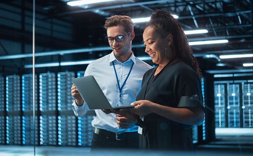 Two technicians collaborating with a laptop in a data center.