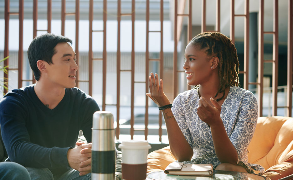 Black woman and Asian man discussing ideas at the office while drinking coffee
